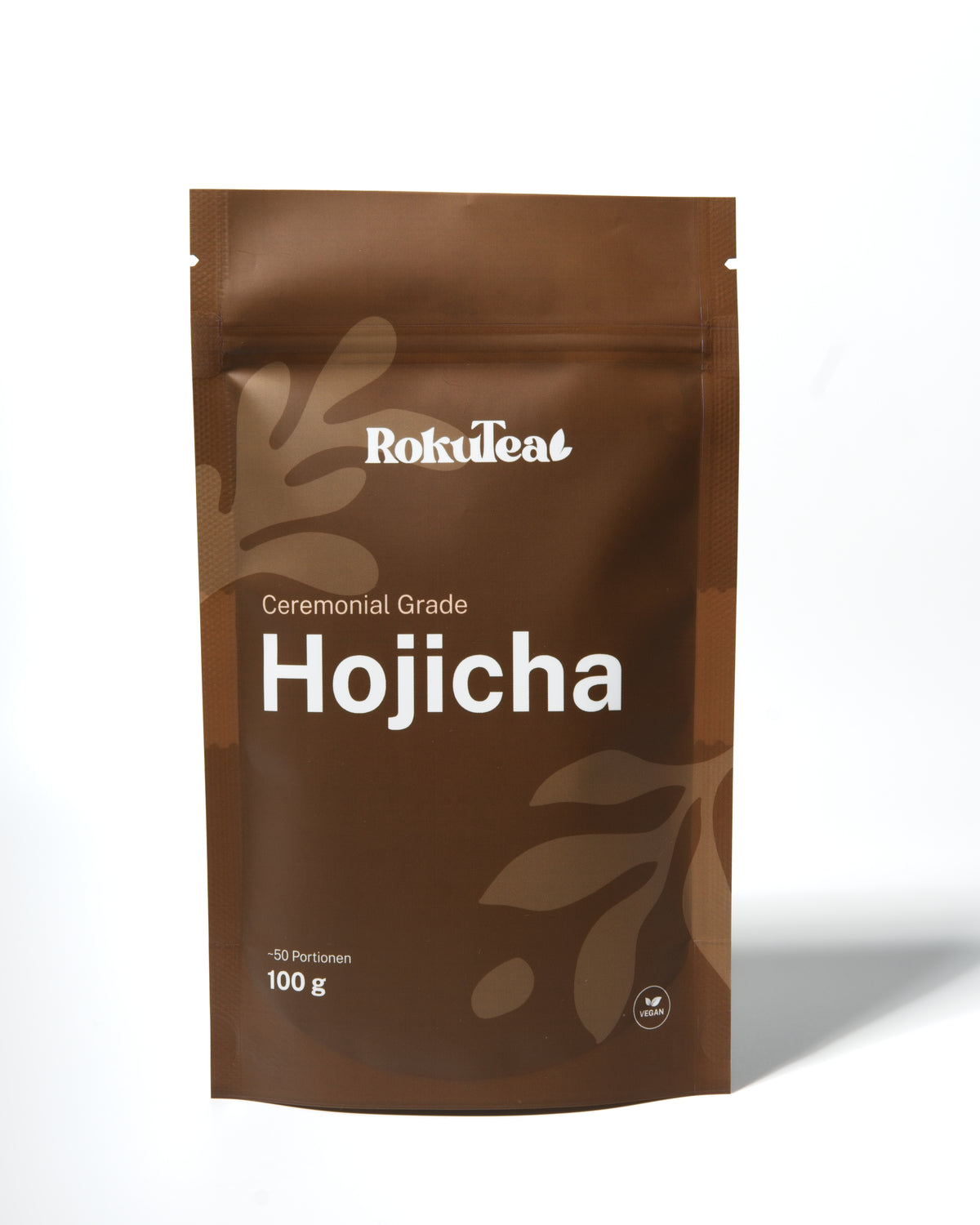 Eine braune RokuTea Verpackung mit der Aufschrift "Ceremonial Grade Hojicha" und "100 g" auf weißem Hintergrund. Die Packung ist als vegan gekennzeichnet.