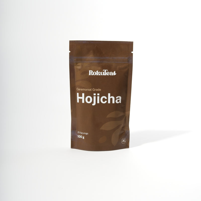 Eine braune RokuTea Verpackung mit der Aufschrift "Ceremonial Grade Hojicha" und "100 g" auf weißem Hintergrund. Die Packung ist als vegan gekennzeichnet.