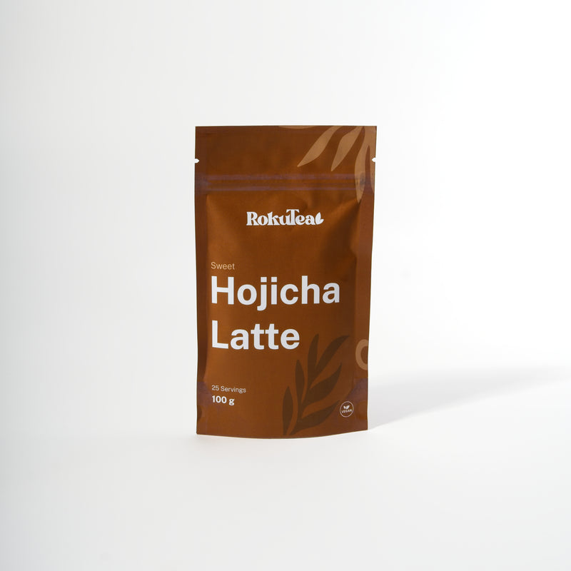 Eine braune RokuTea Verpackung mit der Aufschrift "Sweet Hojicha Latte" und "100 g" auf weißem Hintergrund. Die Packung ist als vegan gekennzeichnet.